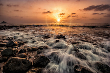 Sunrise at beach with lost of rocks and waves hitting on rocks and slow shutter speed on the water.