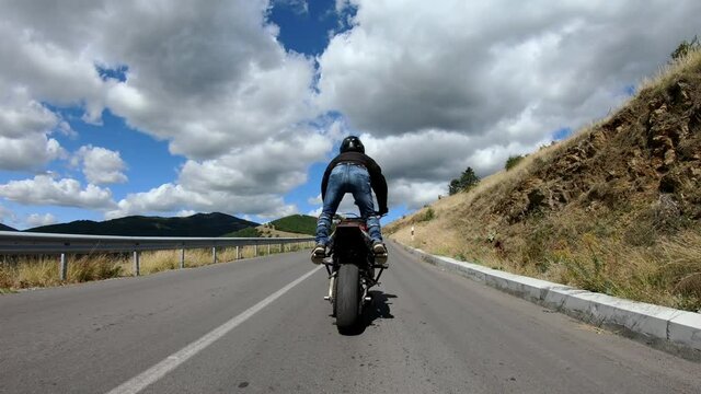 Biker stunt ride biike on mountain rural road and do wheelie on motorcycle