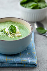 Green cream soup in a blue bowl on a stone grey table