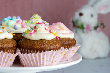 Carrot Cake Cupcakes on a white platter with a stuffed Easter Bunny on the background.