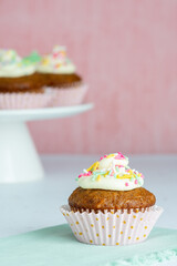 A single Carrot Cake Cupcake in the foreground with a platter of more cupcakes the the background in a vertical format with copy space.