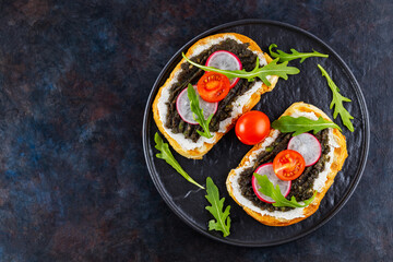 Fototapeta na wymiar Healthy food. Avocado toasts with avocado, cream cheese and radish. Toasts with avocado, arugula and cherry tomatoes on a dark background. Copy space. Top view