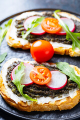 Avocado toasts with avocado, cream cheese and radish. Toasts with avocado, arugula and cherry tomatoes on black plate. Close-up