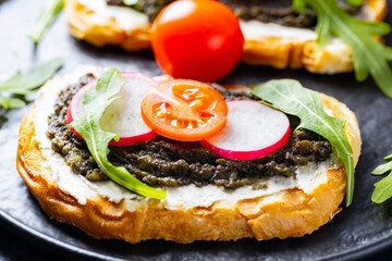 Avocado toasts with avocado, cream cheese and radish. Toasts with avocado, arugula and cherry tomatoes on black plate. Close-up