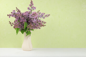 Home interior with decor elements, beautiful spring branches of lilacs in a vase on a light background, abstract flower arrangement, still life with place for text, floral birthday card, wedding,