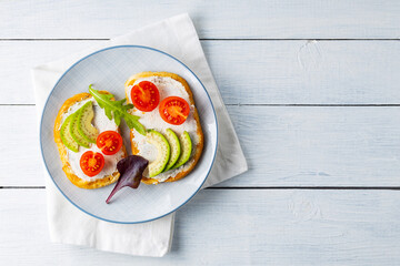 Avocado toasts with cream cheese and cherry tomatoes. Two toasts with avocado and arugula on white boards. Copy space. Top view