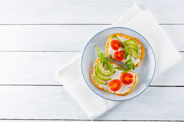 Avocado toasts with cream cheese and cherry tomatoes. Two toasts with avocado and arugula on white boards. Copy space. Top view