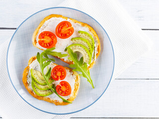 Avocado toasts with cream cheese and cherry tomatoes. Two toasts with avocado and arugula on white boards. Copy space. Top view