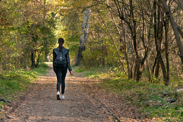 Young woman is walking along the alley of the park. Listening to the nature. Back view.