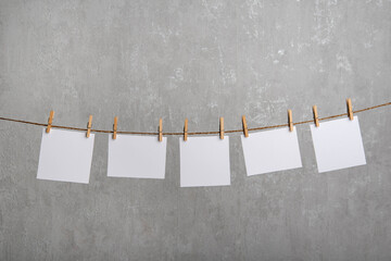 Blank paper notes hang with clothespins on rope. Grey background. Copy space