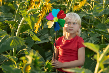 Sad blond boy with a toy windmill in his hands stands on a green field. Eco-friendly