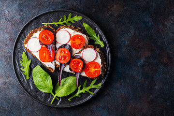 Healthy toasts with cream cheese, cherry tomatoes and spinach on black plate. Bruschetta with cream cheese and fresh herbs on a dark background. Copy space. Top view