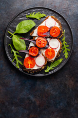 Healthy toasts with cream cheese, cherry tomatoes and spinach on black plate. Bruschetta with cream cheese and fresh herbs on a dark background. Copy space. Top view