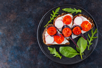 Healthy toasts with cream cheese, cherry tomatoes and spinach on black plate. Bruschetta with cream cheese and fresh herbs on a dark background. Copy space. Top view