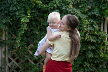 Young beautiful mother hugs and holds child in her arms. Mom and toddler outdoors. Happy motherhood