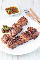 Beef meat skewers with chimichurri sauce, on white plate, vertical
