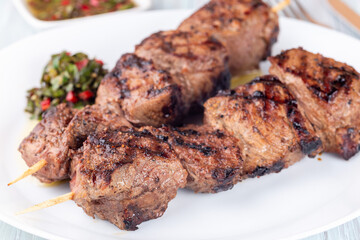Grilled sirloin tips or beef meat skewers with chimichurri sauce, on white plate, horizontal