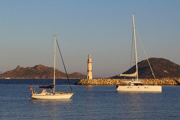 Fototapeta premium Seascape at sunshine. Lighthouse and sailings on the coast. Seaside town of Turgutreis and spectacular sunshine. 
