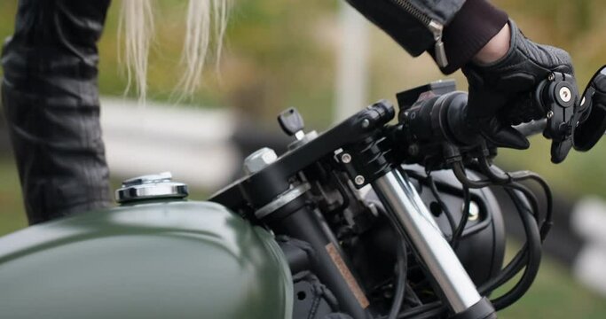 Girl biker takes the wheel of a motorcycle and starts it using the pedal, close-up.