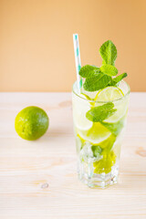 Mojito cocktail in a tall glass. Summer cocktail, lime and wooden juicer on a golden background. Refreshing drink with lime, mint and ice