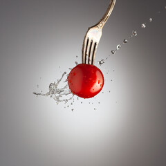 ripe cherry tomato on a fork poured water, water splashes, black white background, gradient
