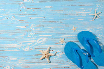 Sea stars and rubber beach blue flip flops on blue wooden background