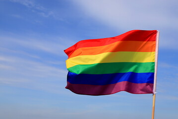 Waving gay pride rainbow flag in blue summer sky. Bright flag of the LGBT community for lesbian, gay, bisexual, transgender.