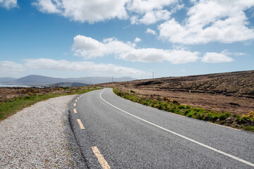 Fototapeta na wymiar Narrow asphalt road on a warm sunny day, beautiful cloudy sky, nobody. Achill island, county Mayo, Ireland. Travel concept