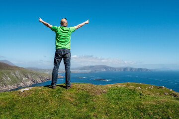 Fototapeta na wymiar Bald male tourist standing on top of a mountain with spectacular view in the background. Moyteoge Head, Achill island, county Mayo, Ireland. Irish landscape. Sunny day, Travel concept