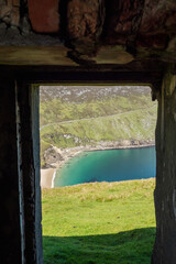 View on Keem beach from a door of an old building. Achill island, county Mayo, Ireland. Beautiful sandy beach with clear blue water. Bright nature landscape framed by dark building
