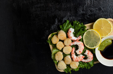 Fototapeta na wymiar Fried scallop with boiled shrimp tail on a salad leaf with soy sauce and wasabi on a dark background in a wooden plate.