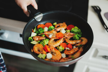 Woman cooking vegetables and shrimps on pan