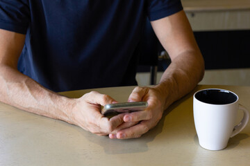 Hands of anonymous man with cellphone on table and coffee cup on side. Stressful lifestyle, busy work, nervous concepts