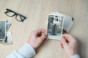 closeup male hand holding old vintage photos of 1940-1950, glasses on the table, concept of family tree, genealogy, childhood memories, memory of ancestors