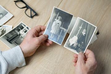 closeup male hand holding old vintage photos of 1940-1950, glasses on the table, concept of family...