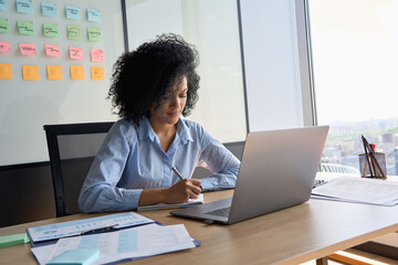 Young African American focused female ceo data analyst businesswoman sitting at desk with laptop...
