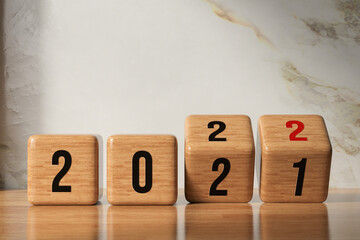 cube turns from 2021 to 2022 on wooden base and marble background - obrazy, fototapety, plakaty