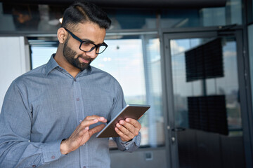 Young indian marketing business manager expert in glasses standing in modern corporate office using...