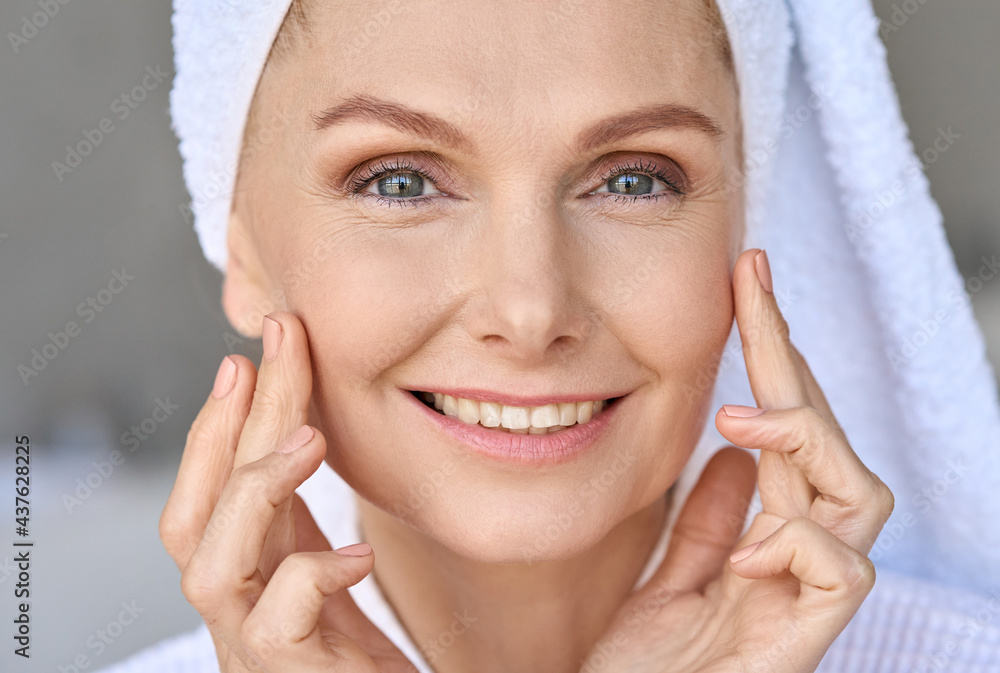 Canvas Prints Closeup portrait of happy smiling gorgeous middle aged woman wearing bathrobe and white towel with perfect complexion touching face looking at camera in bathroom. Advertising of skincare cosmetology.