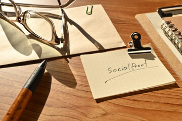 There is a piece of paper with the word Social Proof on the desk with a glasses and clipboard.
