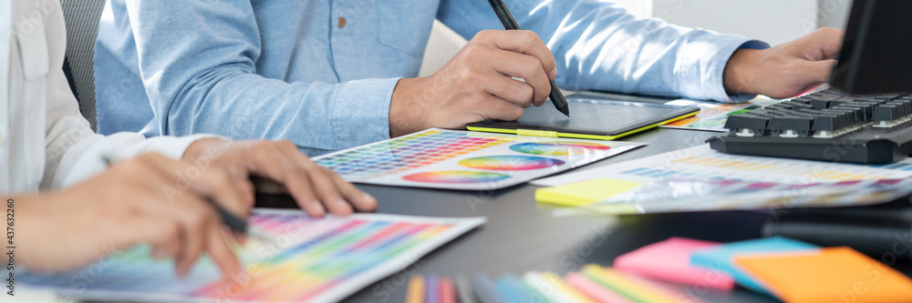Poster graphic designer or creative working together coloring using graphics tablet and a stylus at desk wi