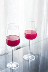 High angle of two crystal glasses with red wine on a glass table and soft backlighting in a living room window