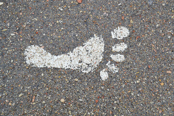 White paint imprint of a human footprint of bare feet on an asphalt road. White foot print.