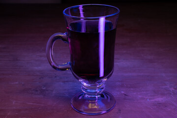 Cappuccino glass cup with dark liquid and neon uv lights on a wooden table