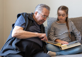 Grandpa is looking at a photo album with his little granddaughter.