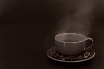 cup of coffee with beans, aroma​, hot​ steam​ from​ black​ coffee​ on​ dark​ and​ blur​ scene​