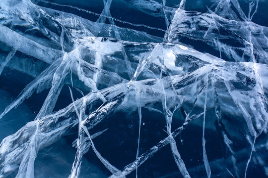 Many cracks in the blue ice. Natural texture of transparent clear ice of the lake. Horizontal.