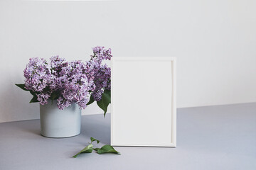 Mock up photo frame in minimalistic interior. Modern still life scene of white frame and bouquet of lilacs. Concept trendy home decor. Banner in pastel colors.