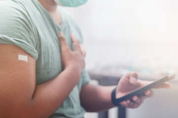 Youngman wearing a protective mask Show plaster on the shoulder Use your smartphone to find information about the impact of post-vaccination against covid-19, health care guidelines, health protection