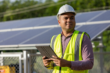 Young asian electrical engineer standing in front of Solar cell panels farm. He using tablet to...